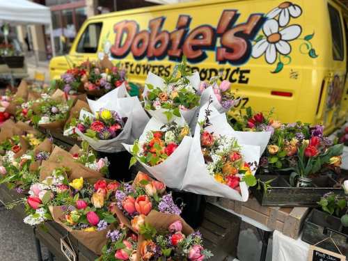 A vibrant flower stand with colorful bouquets in front of a yellow van labeled "Dobie's Flowers & Produce."