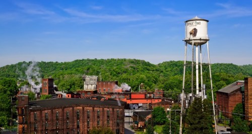 A scenic view of a factory complex with a water tower, surrounded by lush green hills and blue skies.