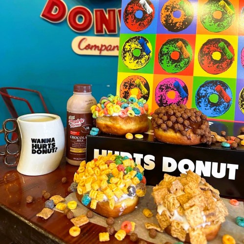 A colorful display of donuts topped with cereal, a coffee mug, and a chocolate drink on a wooden table.