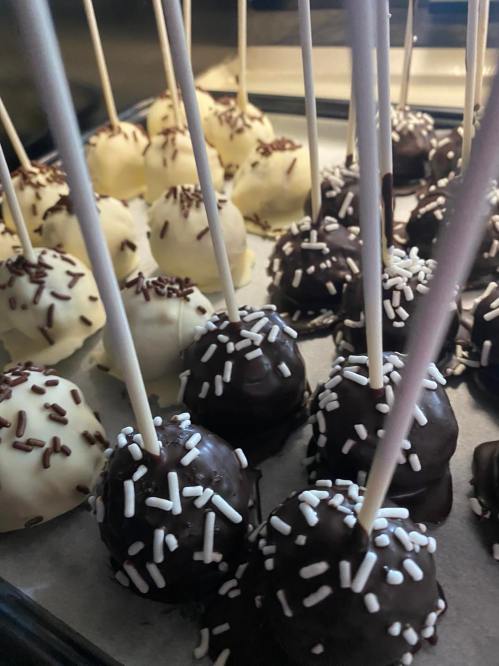 A tray of cake pops coated in white and dark chocolate, topped with sprinkles and placed on parchment paper.