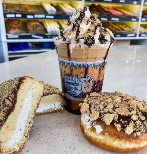 A creamy dessert drink topped with whipped cream, alongside two donuts: one filled with cream and another with a crumb topping.