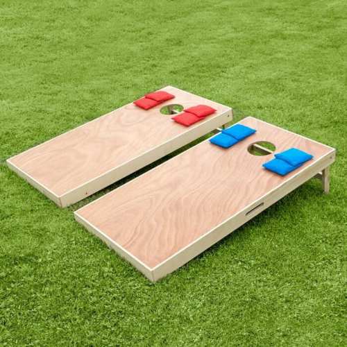 Two cornhole boards on green grass, each with a hole and colored bean bags—red and blue—ready for play.