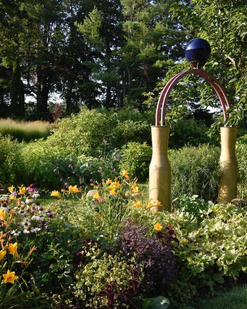 A colorful garden featuring vibrant flowers and a decorative arch with a blue sphere on top, surrounded by lush greenery.