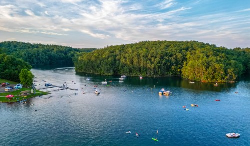 A scenic lake surrounded by lush greenery, with boats and kayakers enjoying the water on a sunny day.