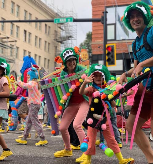 A colorful parade scene with people in vibrant costumes, playing instruments and wearing fun monster hats.