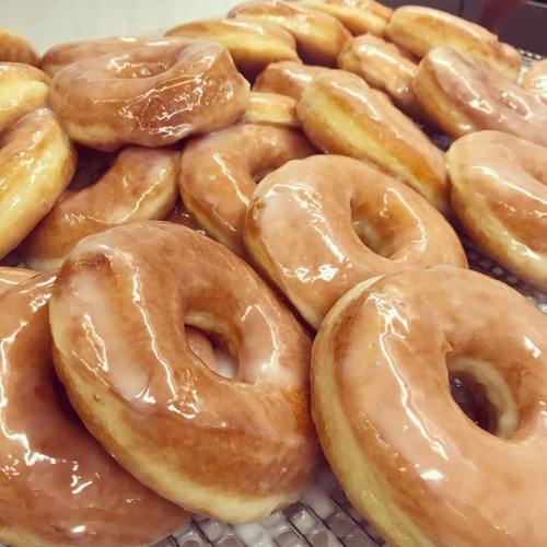A close-up of freshly glazed donuts stacked on a cooling rack, glistening with a sugary glaze.