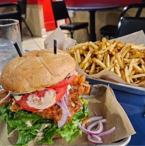 A crispy chicken sandwich with lettuce, tomato, and onion, served with a side of golden fries on a blue table.