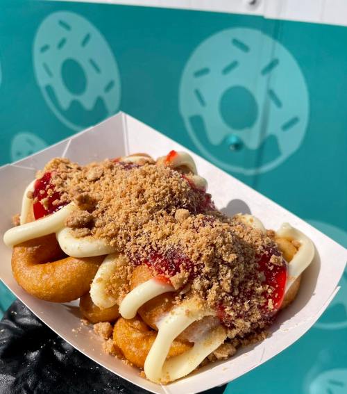 A tray of mini donuts topped with cream, strawberry sauce, and crumbled cookies against a teal background.