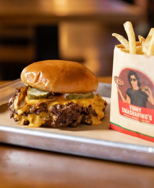 A juicy cheeseburger with pickles on a bun, served with a side of crispy fries in a branded container.