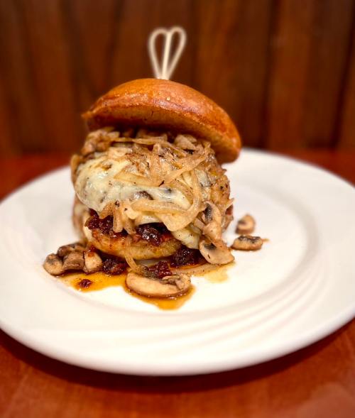 A gourmet burger topped with melted cheese, sautéed onions, and mushrooms, served on a toasted bun.