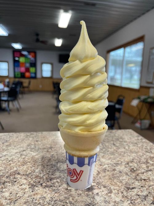 A tall, swirled soft serve ice cream cone on a countertop, with a cozy indoor setting in the background.