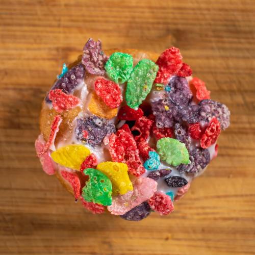 A colorful donut topped with a variety of fruity cereal pieces on a wooden surface.