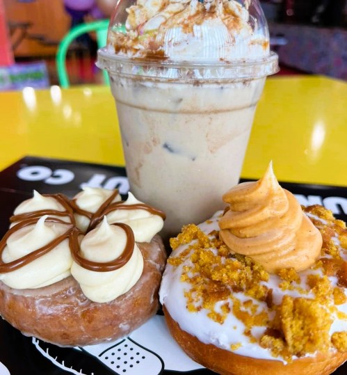 A colorful table with two donuts topped with frosting and a creamy drink in a cup with whipped cream.