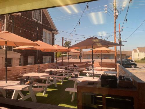 Outdoor dining area with picnic tables and umbrellas, surrounded by wooden fencing and string lights on a sunny day.