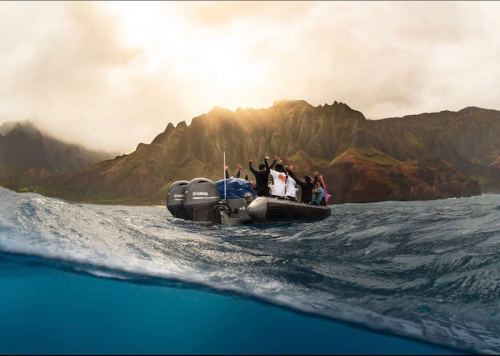 A group of people on a small boat in the ocean, with mountains and a dramatic sky in the background.