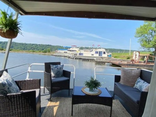A cozy seating area on a boat, overlooking a calm river with other boats docked in the background.