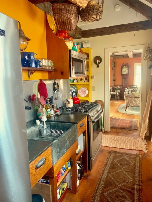 Cozy kitchen with yellow walls, stainless steel appliances, wooden cabinets, and a view into a living room.