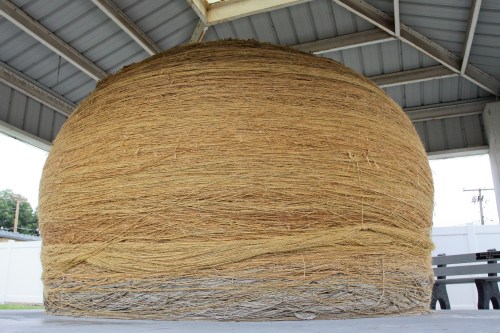A large, round structure made of tightly wound straw or fibers, displayed under a metal roof.