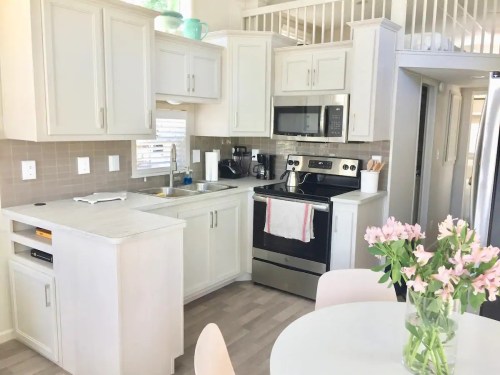 Bright kitchen with light cabinets, stainless steel appliances, and a dining table with a vase of flowers.