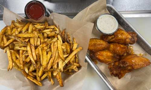 A tray with crispy fries and a side of chicken wings, accompanied by dipping sauce and a small cup of ketchup.