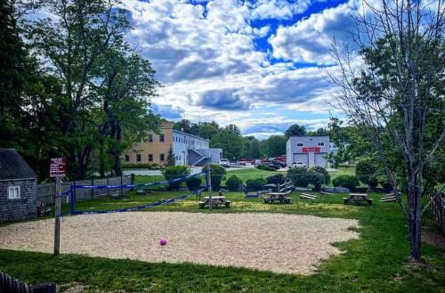 A sandy volleyball court surrounded by trees and picnic areas under a partly cloudy sky.