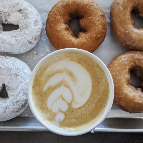 A cup of latte art sits in front of four assorted donuts on a tray.