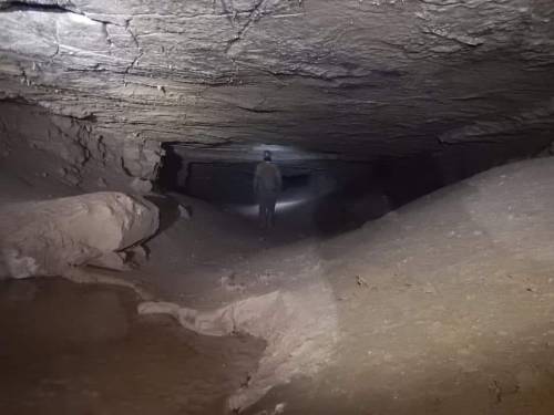 A person walking through a dimly lit cave with rocky walls and a small pool of water on the ground.