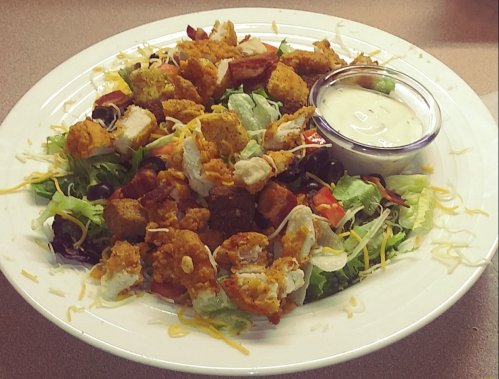A colorful salad topped with crispy chicken, cheese, and a side of ranch dressing.