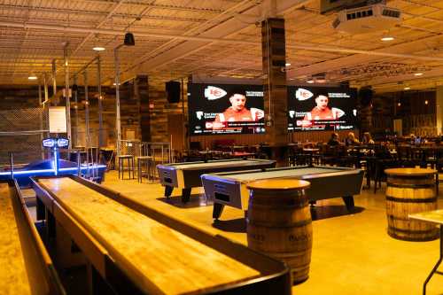 A spacious bar with pool tables and large screens showing a sports game, featuring wooden decor and seating areas.