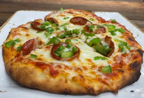 A close-up of a pizza topped with pepperoni, melted cheese, and chopped green peppers on a white plate.