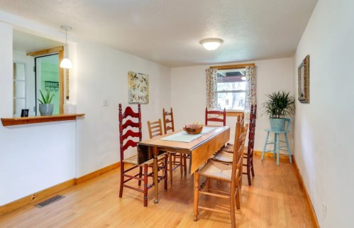 A bright dining area with a wooden table, eight chairs, and a small bar area, featuring light walls and natural decor.