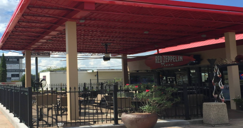 Exterior of Red Zeppelin Pizza with a covered patio, outdoor seating, and a sign visible in the background.