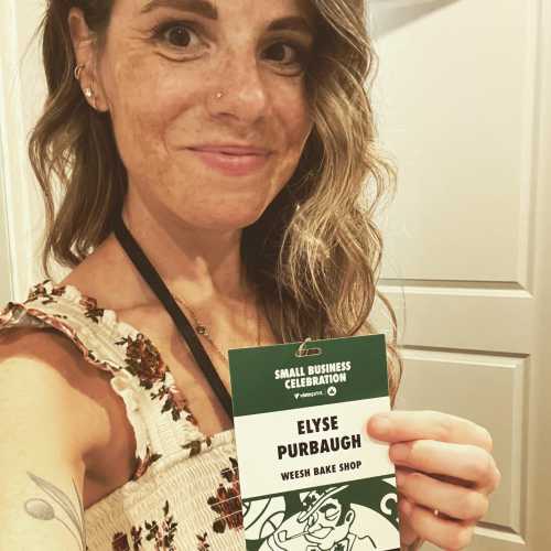 A woman with wavy hair holds a name tag for Elyse Purbaugh at a small business celebration event.