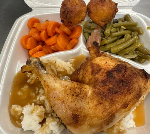 A takeout container with fried chicken, rice and gravy, carrots, green beans, and two cornbread muffins.
