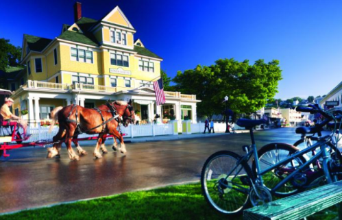 A horse-drawn carriage passes by a yellow Victorian house, with bicycles parked nearby and a clear blue sky above.