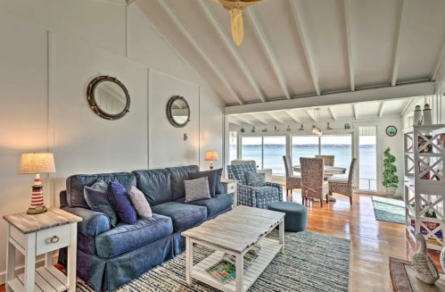 Cozy living room with blue sofa, wooden coffee table, and large windows overlooking a scenic view. Bright and inviting space.