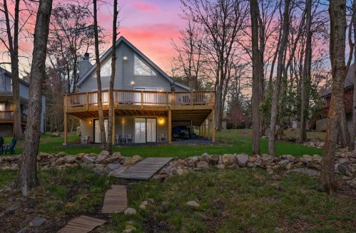 A cozy cabin with a large deck surrounded by trees, set against a colorful sunset sky.
