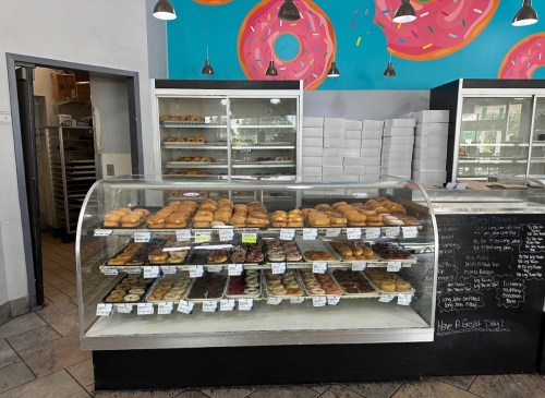 A display case filled with various donuts and pastries, with a colorful donut-themed mural in the background.