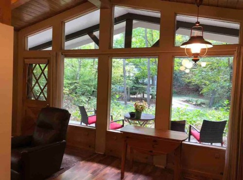 Cozy interior with large windows overlooking a lush green garden and outdoor seating area.