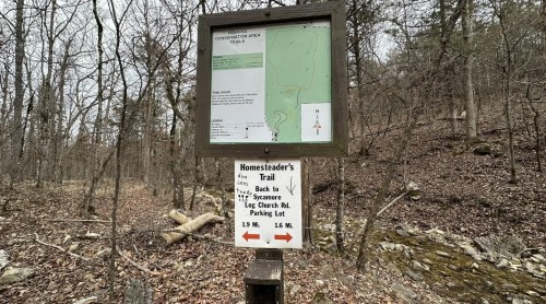Trail map sign in a wooded area, showing routes for Homesteader's Trail and directions to the parking lot.