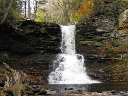 A serene waterfall cascading over rocky cliffs, surrounded by autumn foliage and a tranquil pool below.