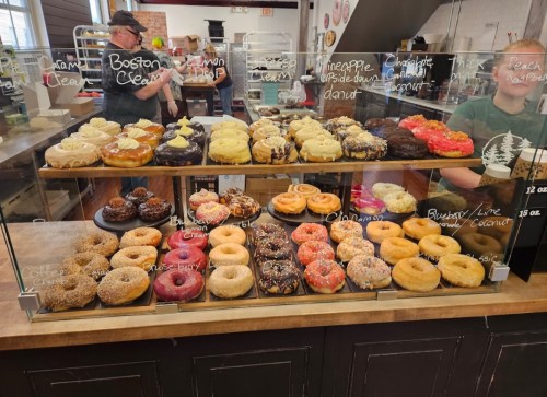 A display case filled with a variety of colorful donuts, including Boston cream, chocolate, and fruit-flavored options.