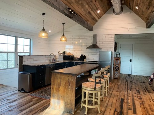 A modern kitchen with wooden beams, a long island, bar stools, and stainless steel appliances in a bright, open space.