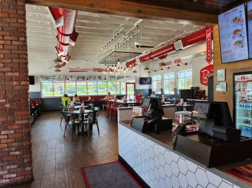 Bright, modern restaurant interior with red accents, tables, and a counter area. Large windows let in natural light.