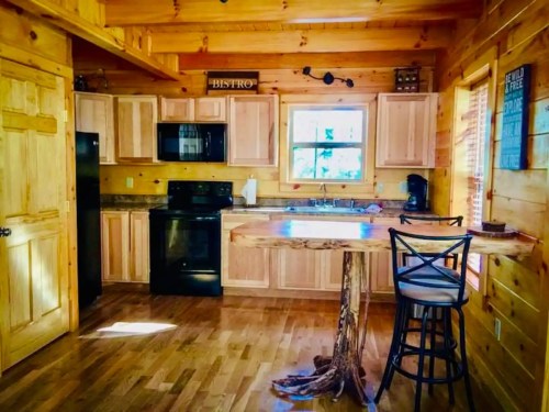 Cozy wooden kitchen with a rustic table, black appliances, and natural light from a window.