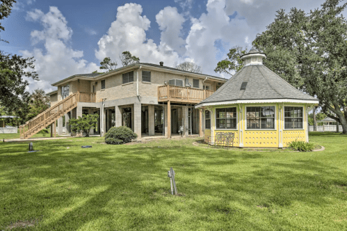 A two-story house with a wooden deck and a yellow gazebo in a green yard under a partly cloudy sky.