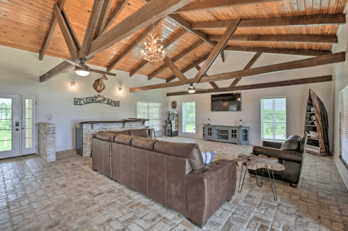 Spacious living room with wooden beams, a stone fireplace, and large windows, featuring a cozy sofa and modern decor.
