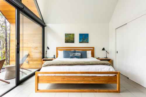 A modern bedroom featuring a wooden bed, decorative pillows, and large windows with a view of nature.