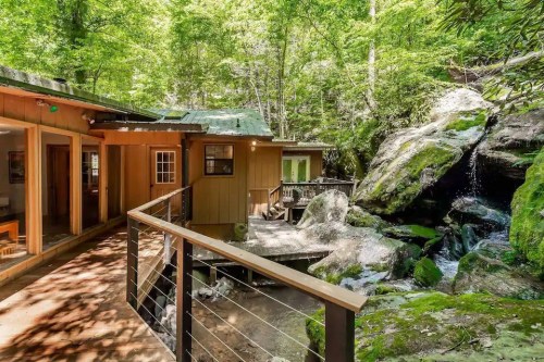 A wooden cabin nestled in a lush forest, with a small waterfall and rocky landscape nearby.