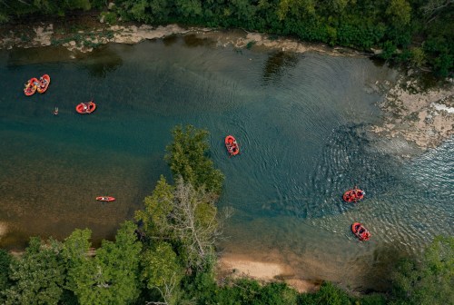 Aerial view of a river with several red rafts and people enjoying a day of rafting among lush green trees.
